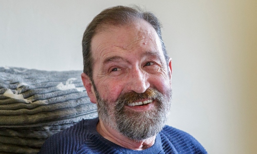 An older man with a beard smiles off camera