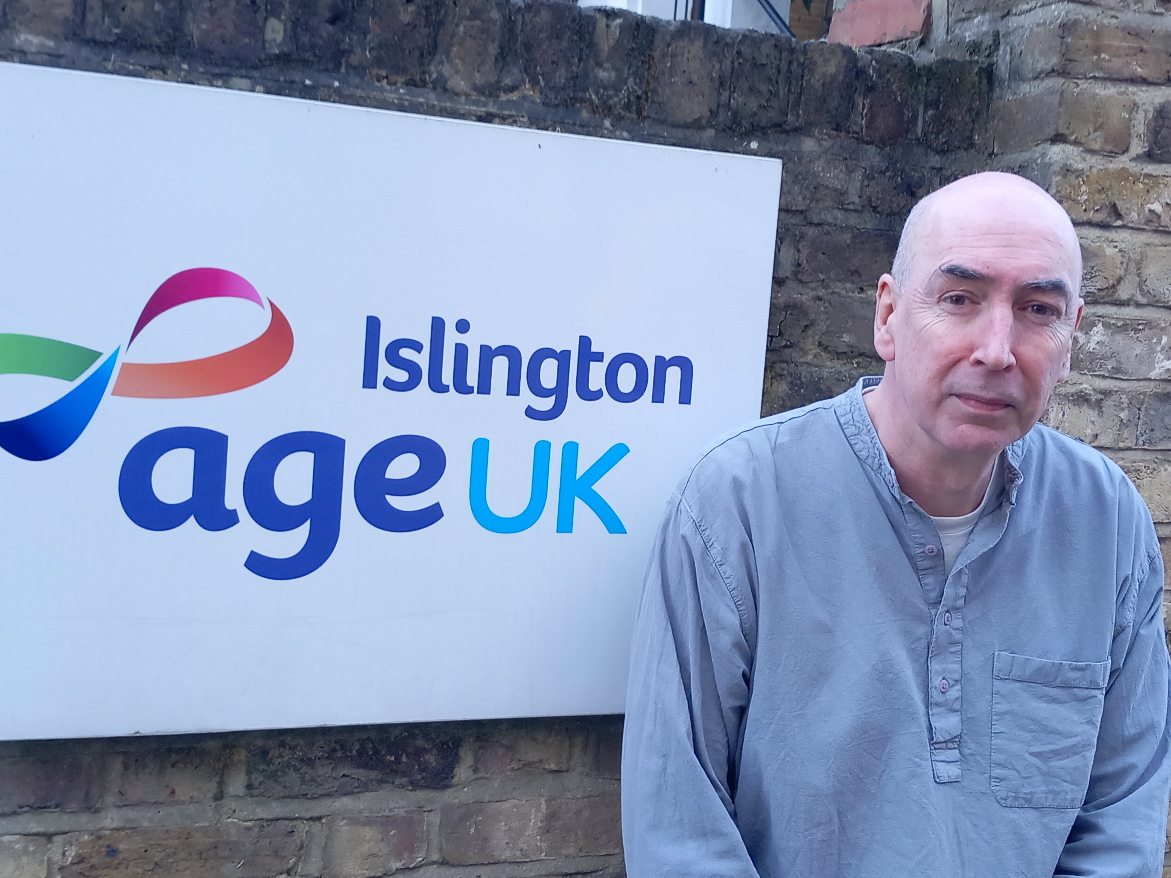 man standing outside Age UK Islington offices and sign