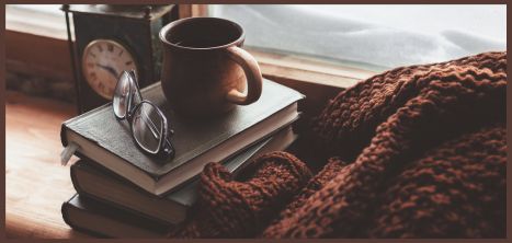 Coffee cup on a pile of books with pair of reading glasses and a brown blanket