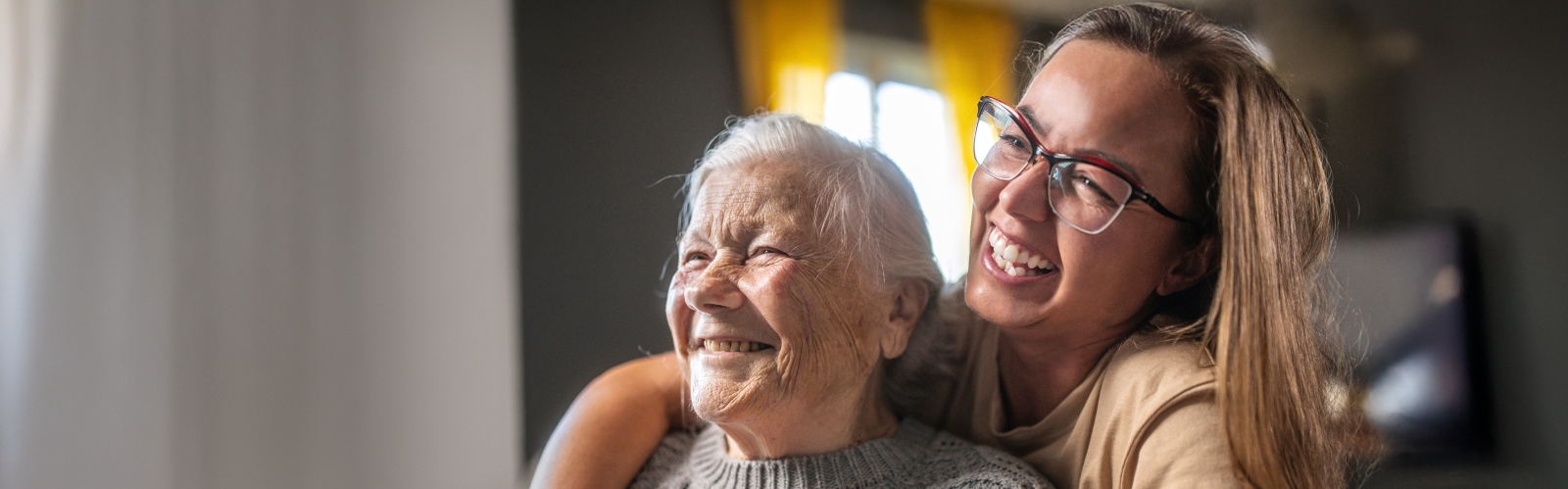 An older woman is hugged by her daughter, while both laugh