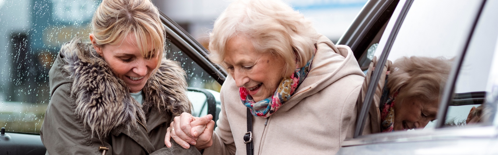 A young woman helps an older woman out of a car