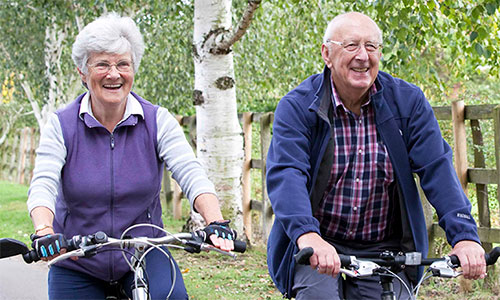 An older couple, a man and a woman, ride bikes alongside one another
