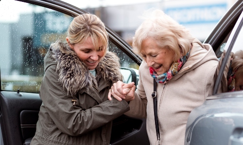 A young woman helps an older woman out of a car
