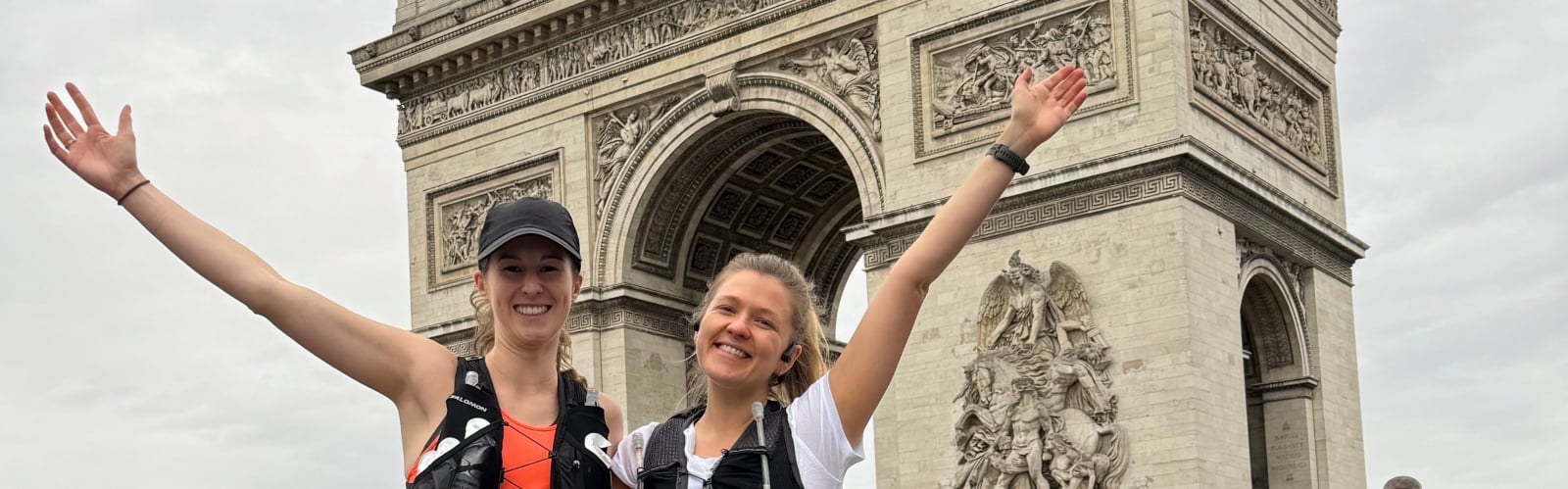 Two women stand smiling in front of the Arc de Triomphe