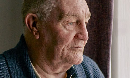 An older man stares sadly out of the window