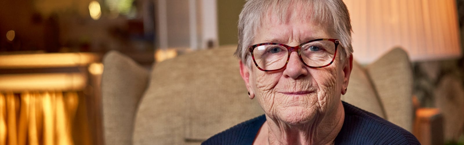 An older woman with glasses and short grey hair smiles at the camera