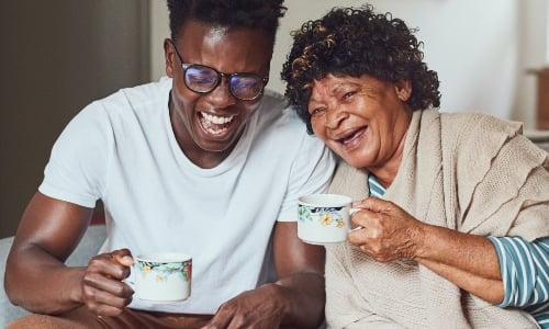 A young man laughs with his grandmother while drinking tea