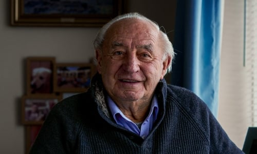 An older man with silver hair smiles at the camera