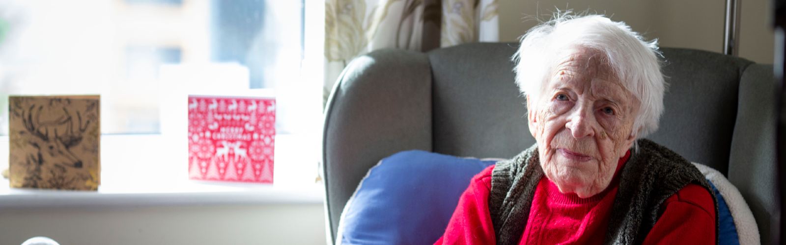 An older woman in a red jumper, looking towards the camera.