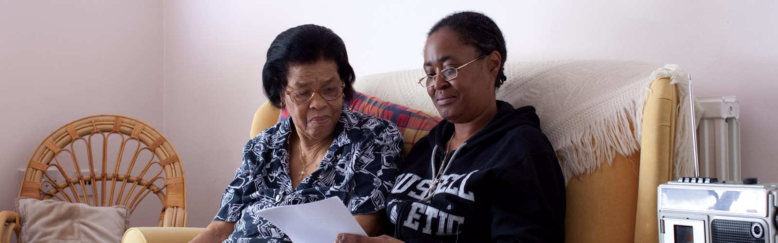 Two ladies sat on a sofa, looking at a piece of paper