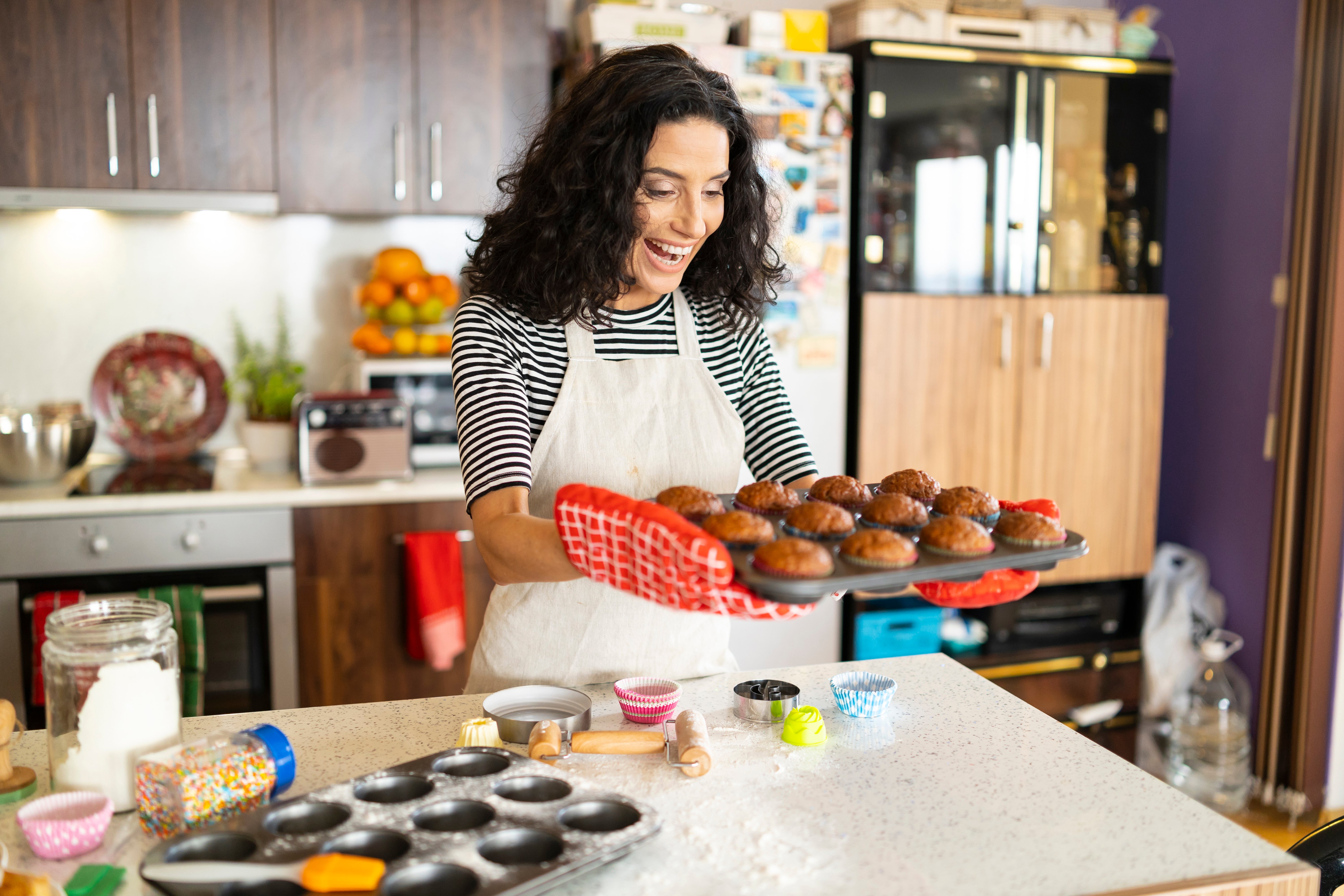 A woman smiling while holding a tray of muffins