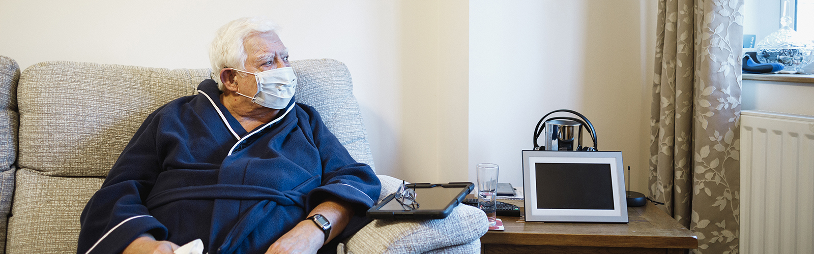 An older man in a mask, sat on a sofa