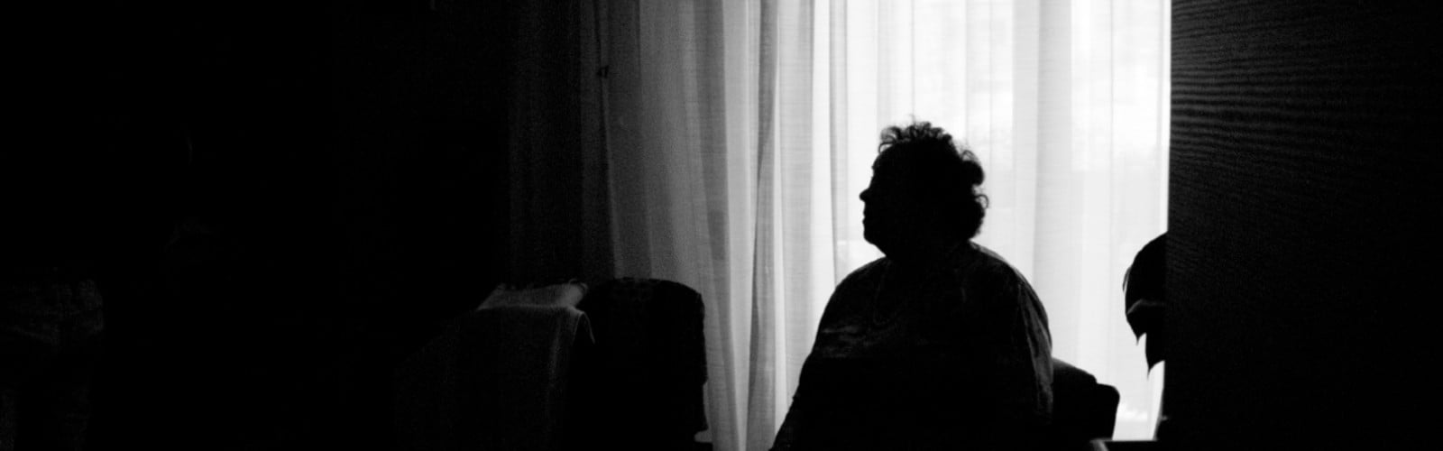 A black and white photo showing a woman sitting in shadow in a room