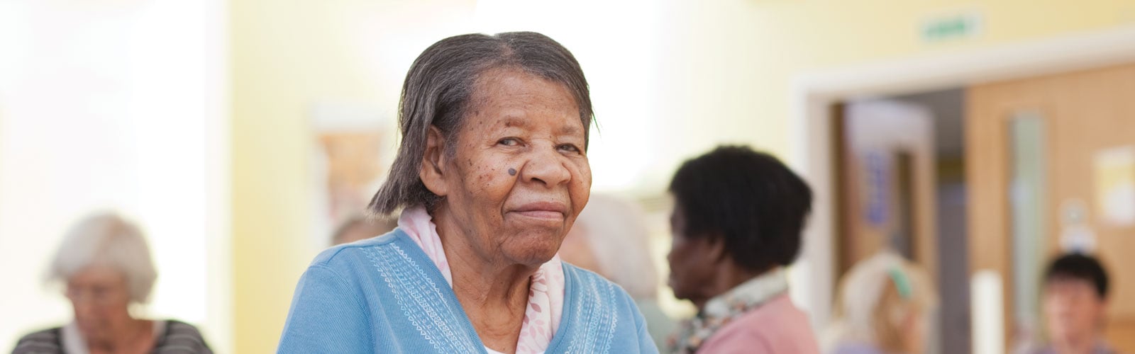 An older lady in a care home, wearing a blue cardigan.