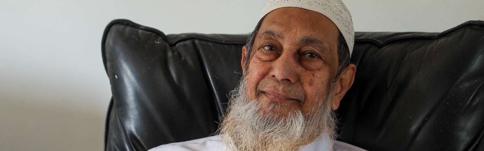 An older man, sat on his sofa smiling at the camera