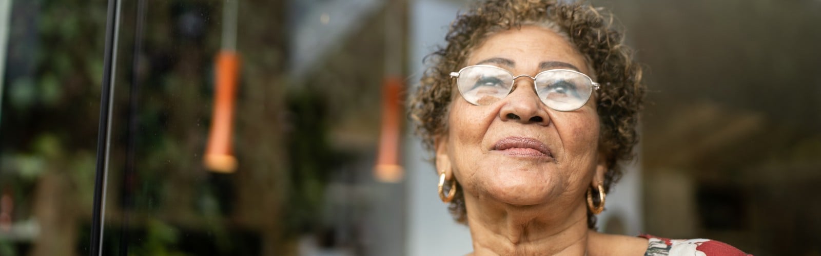 An older lady stood outside a house, smiling.