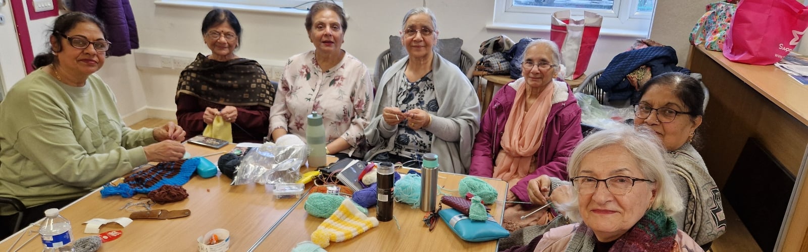 A group of older women, gathered around a table knitting