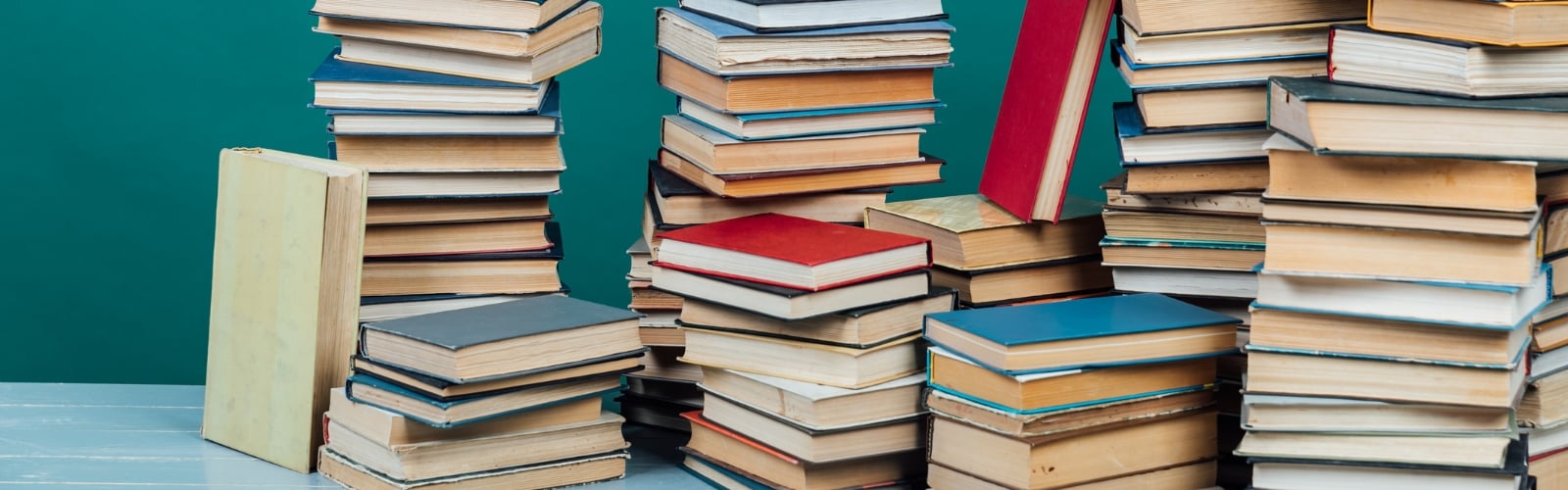 Multiple stacks of books against a teal background