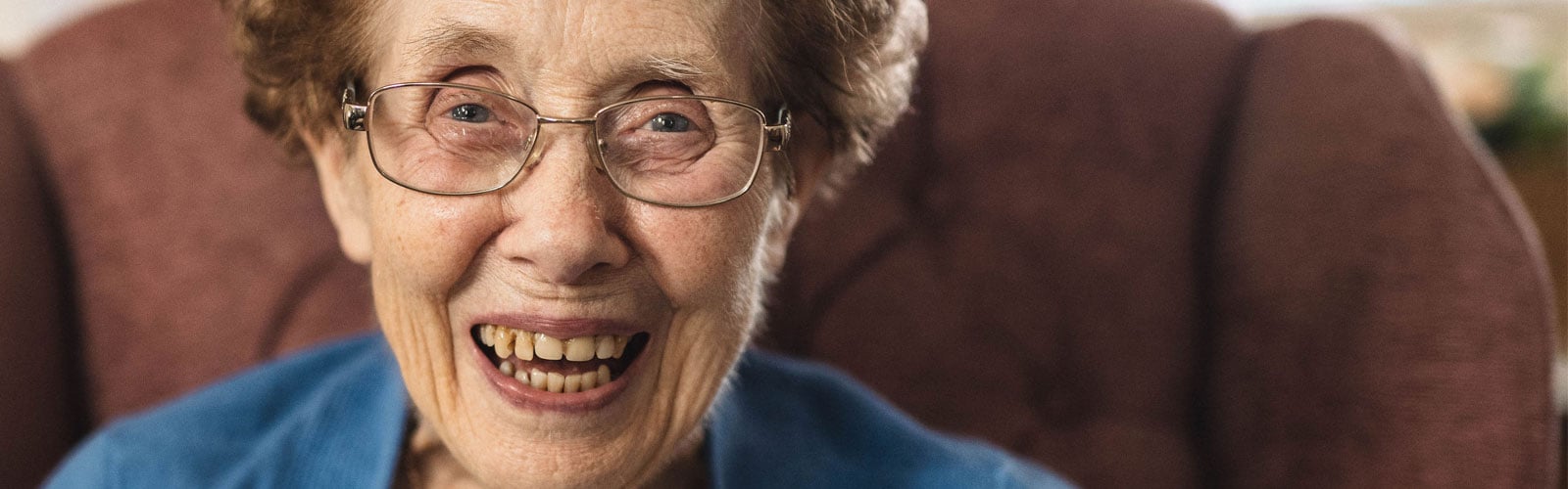 An older lady with reddish hair and glasses grins at the camera