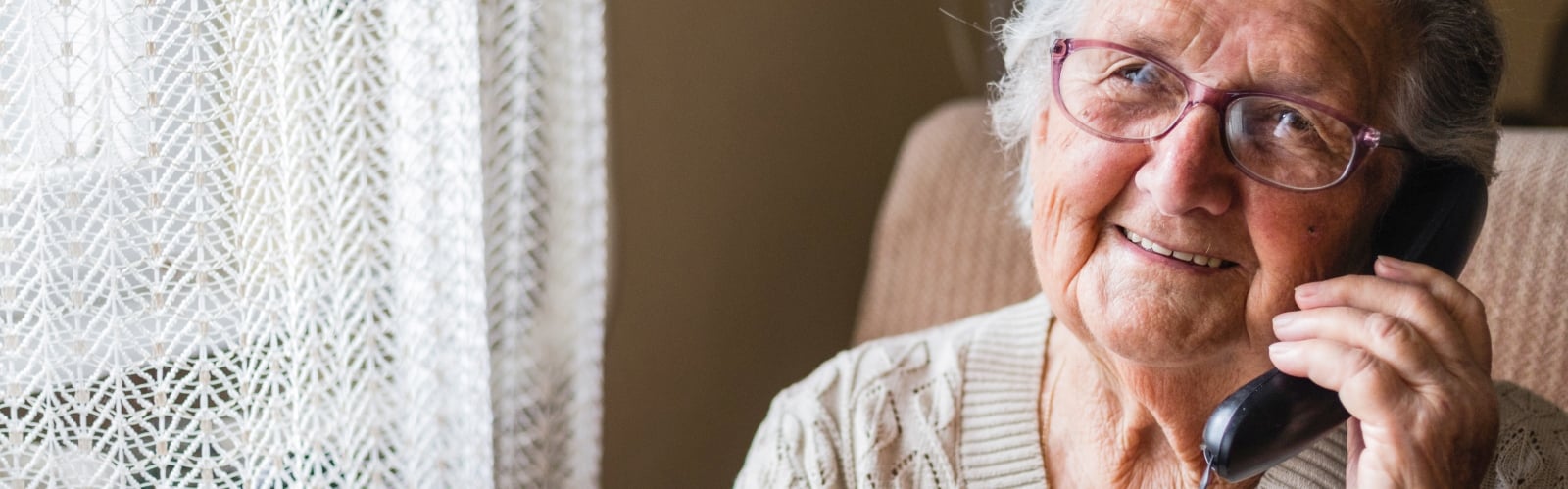 An smiley older woman with grey hair, talking on a landline phone