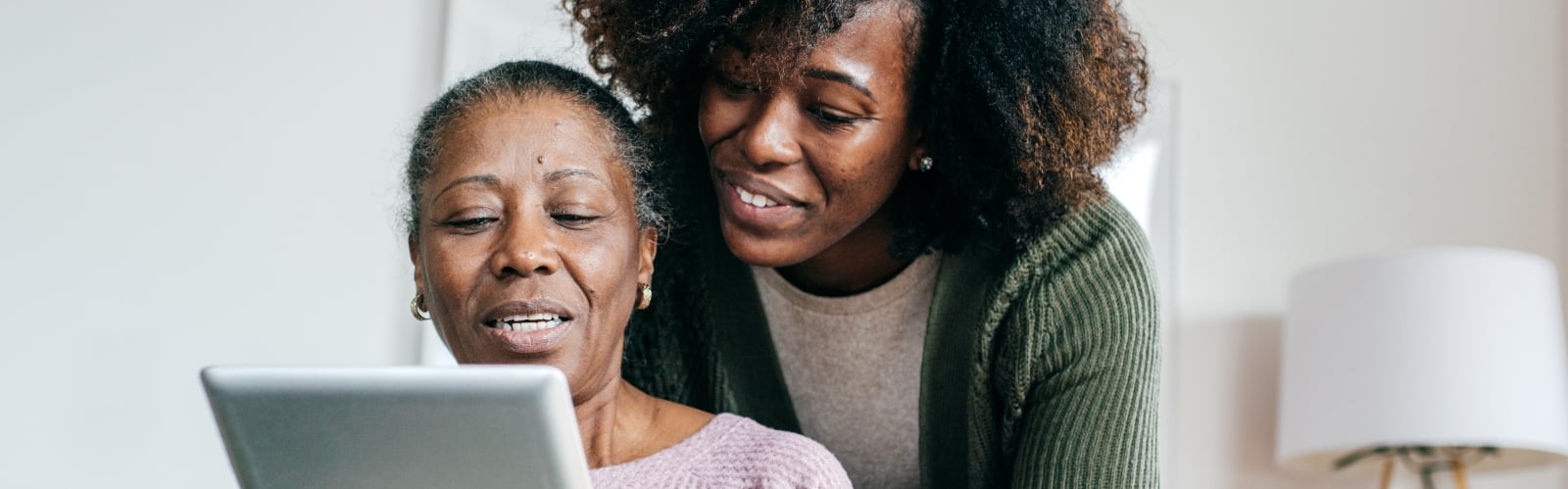 An older woman uses a tablet, helped by her daughter