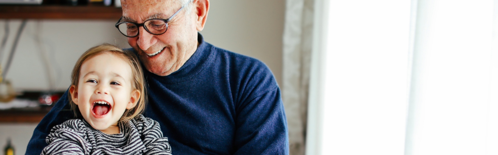 An older man laughs with his grandchild