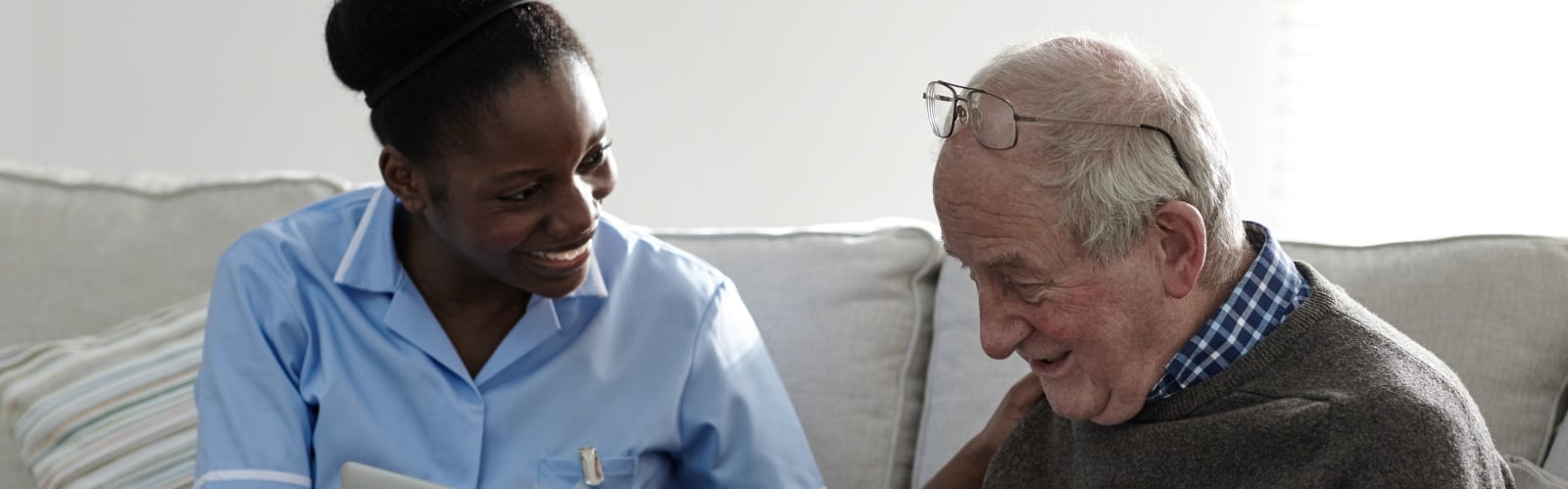 A young Black woman in NHS uniform talks to an older man