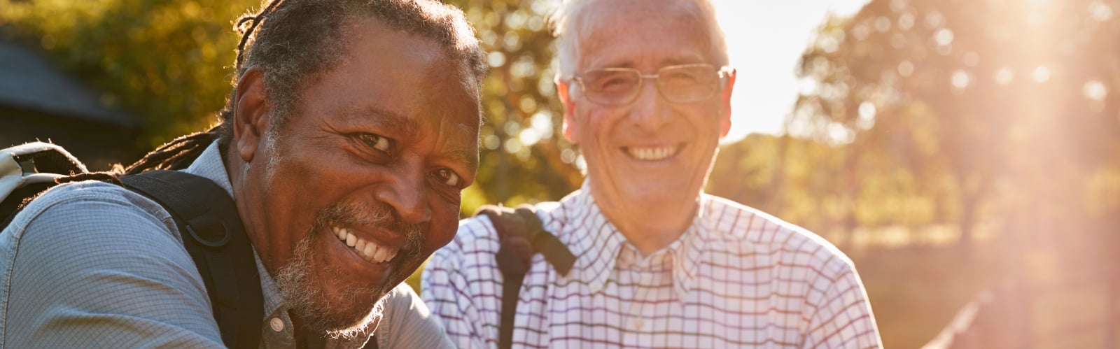 Two older men smile towards the camera, as evening sun shines in the background