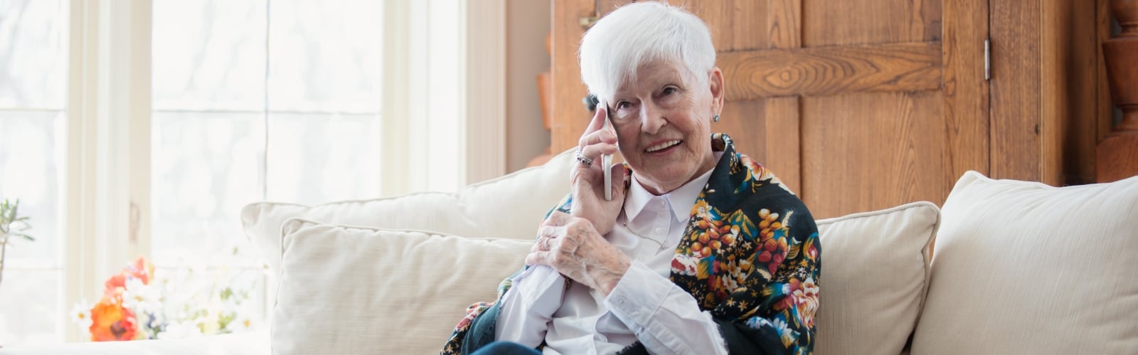 An older lady wearing a shawl sits on a sofa enjoying a phone call