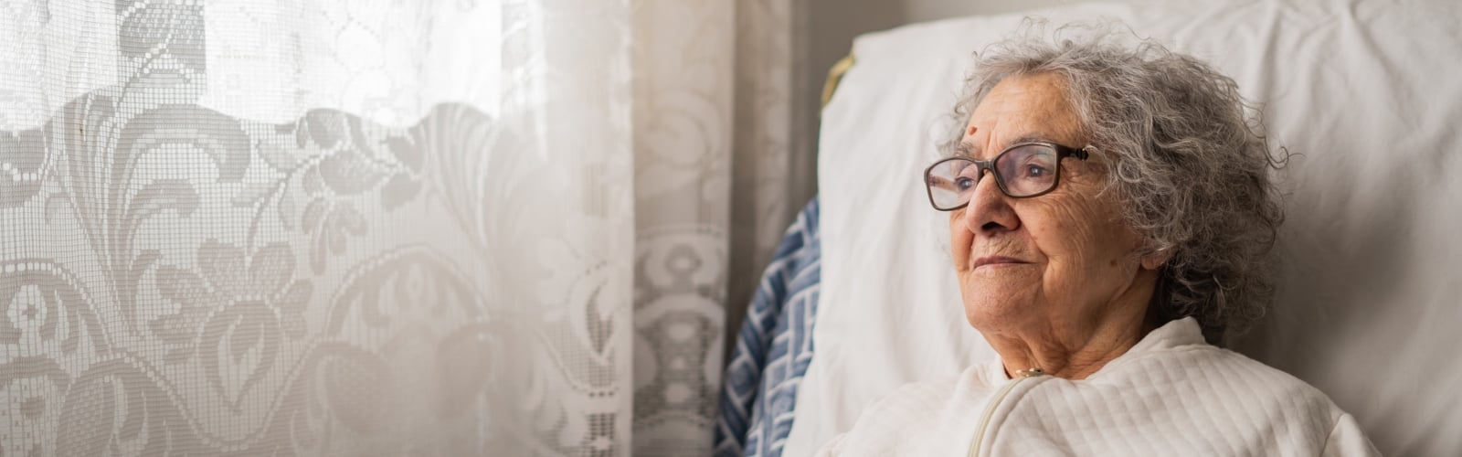 An older woman with glasses looking thoughtfully out of the window