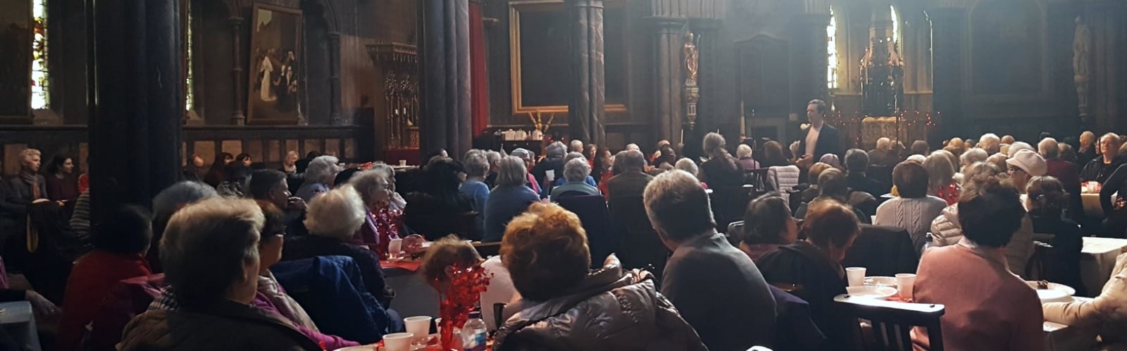 Groups of older people, sat a multiple tables, gathered to watch a performance