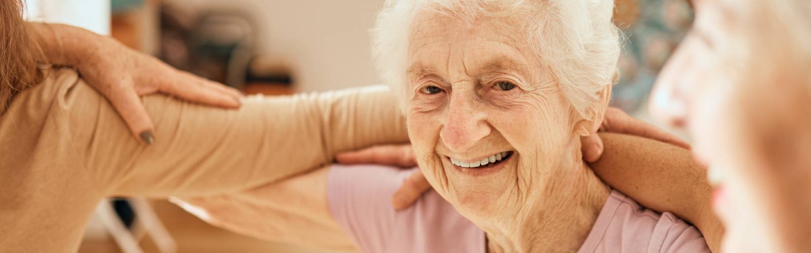 An older lady taking part in a physical activity class, with her arms around others