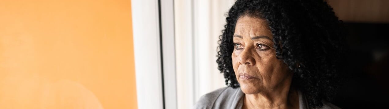 An older Black woman stares thoughtfully out of the window