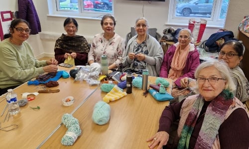 A group of older women, gathered around a table knitting