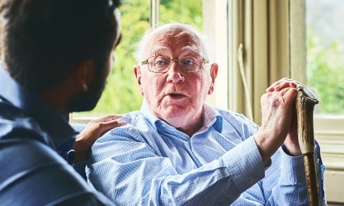 An older man with glasses is comforted by a younger medical professional