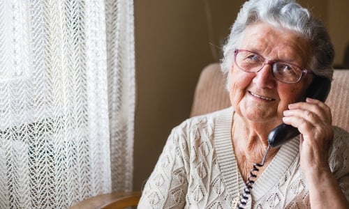 A smiley older woman with grey hair, chatting on her landline phone