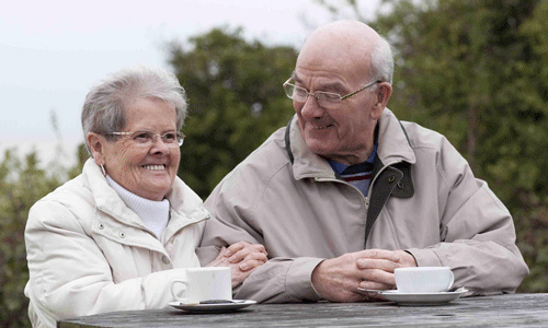 Couple drinking a cup of tea on a picnic table, wrapped up in winter coats