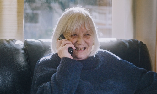 An older woman with a whitish blonde bob laughing on the phone