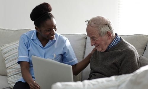 A young Black woman in NHS uniform talks to an older man