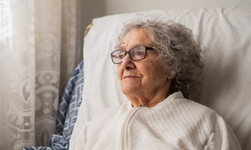 An older woman with glasses looks thoughtfully out of the window