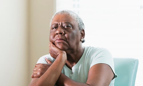 An older woman, sat with her hand underneath her chin.