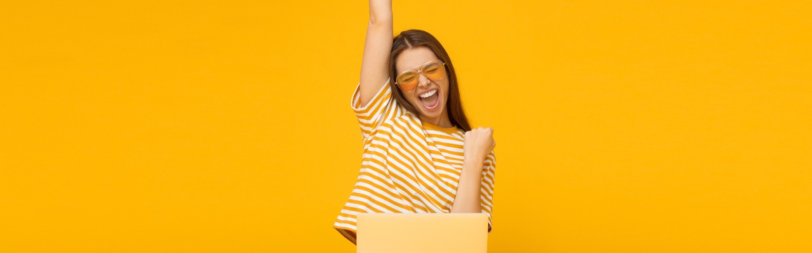 woman sitting in front of a laptop with her hand in the air celebrating a lottery win