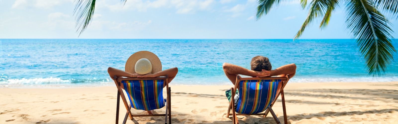 couple relaxing on sun loungers on the beach with palm trees